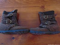 Side view of both brown suede ankle boots showing buckle straps, zipper side, and rubber soles