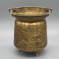 Front view of brass planter showing embossed design, copper handle, tripod feet