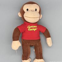 Front view of Curious George plush showing overall appearance, shirt, face, and tag