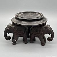 Front view showing three carved elephants supporting round top