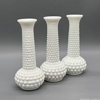 Three white hobnail milk glass bud vases standing upright