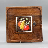 Front view of wood tray displaying inset fruit tile and finger hole