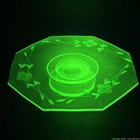 Plate glowing bright green under UV light showing uranium content and etched floral pattern.