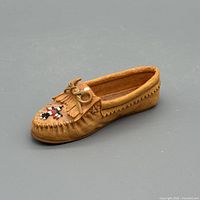 Side view of tan moccasin figurine showing fringe, beading, lace