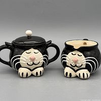 Front view of both cat-shaped ceramic pieces: lidded sugar bowl and creamer