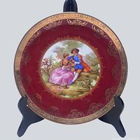 Full view of plate showing burgundy rim, gold gilding, central scene