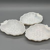 Three white milk glass dishes grouped, showing overall shape and motif