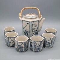 Teapot with lid and handle fronted by six cups