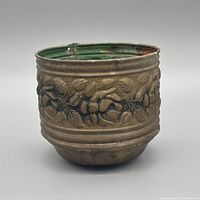 Side view of round embossed copper and tin cachepot showing botanical motif and patina