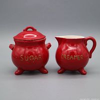 Front view of sugar jar with lid and creamer showing lettering and tripod feet