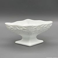 Front view of square milk glass compote showing floral embossing and pedestal base