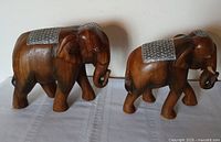 Side view of both wooden elephants displaying size difference and silver plates