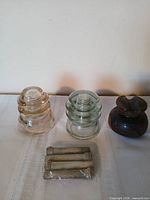 Group view of two glass insulators, one brown porcelain insulator and bag of four knob-and-tube sleeves