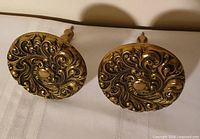 Front view of both ornate brass tiebacks showing medallion design