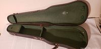 Open violin case showing green felt interior and accessory compartment