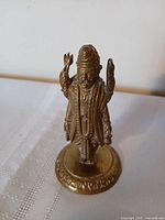 Front view of brass Hindu deity figurine showing crown, raised hand and base