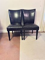 Front view of both black faux leather dining chairs showing overall design