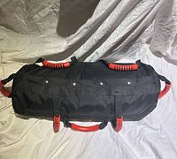 Full view of black sandbag showing cylindrical shape and multiple red handles