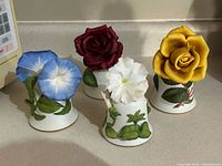 Front view of four bone china bells with blue morning glory, red rose, white petunia, yellow rose