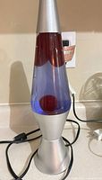 Full view of lava lamp showing silver base, glass vessel with red wax in purple liquid