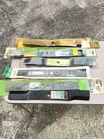 Six packaged lawn-mower blades laid out on table