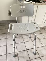 Front view of shower chair showing seat, backrest with writing, and height-adjustable legs