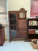 Front view of closed cabinet showing glass door, mirror, drop front closed