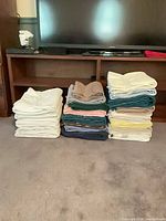 Three stacks of assorted bath towels in various solid colours on floor