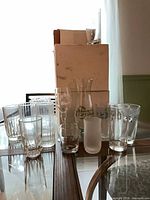 Group of assorted clear and frosted glasses on table including ribbed tumblers, rocks glass, frosted tumbler, Pat O'Brien's carafe and goblet