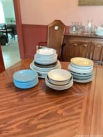 Four stacks of assorted plates and bowls in white, light blue and cream colors on wooden table
