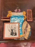 All items laid out on surface including framed tile, wood pieces, pennants in plastic, resin figurine