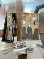 Overall lot view showing packaged set, white-handled bundles, and tray of loose cutlery