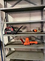 Shelf showing both hedge trimmers, battery and charger