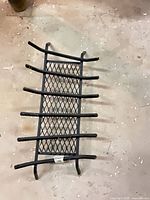 Top view of black steel fireplace grate showing mesh base and five support bars