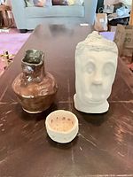 Group shot of brown glazed vase, white head sculpture, white pierced pinch pot on table
