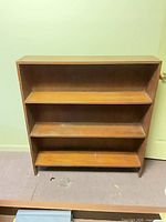 Front view of brown veneer bookcase showing three shelves and overall wear