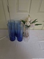 Group shot of four blue vases beside clear vase with flowers