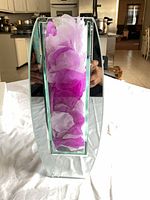 Front view of curved clear glass vase filled with purple and white tissue paper