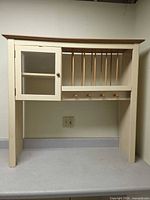 Full front view of cream wall cabinet with glass door, plate rack, peg hooks