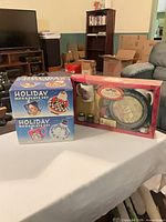 All three boxed sets displayed: two blue Holiday mug & plate sets and one red Currie & Tres tray & mug set
