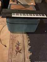 Full view of synthesizer on stool with power cable visible