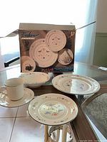 Box showing Fashion House Homecoming dinnerware, one cup and three plates displayed