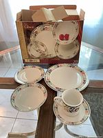 Set displayed with dinner plates, salad plates, bowls, saucer and mug in front of original box