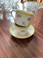 Two teacups stacked on saucer showing floral pattern and yellow rims