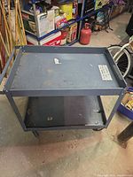 Full view of gray metal utility cart showing two shelves, handle and casters