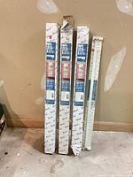 Four boxed Kirsch traverse rods standing against wall; visible box damage