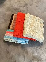 Three folded blankets stacked showing cream, orange, multicolor edges