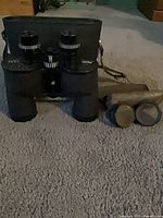 Binoculars standing in front of hard case with lens caps and strap visible