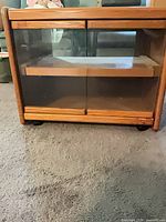 Front view of oak veneer TV stand with glass doors and casters