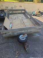 Front quarter view showing wooden stake sides, plywood floor, tongue and damaged wheel